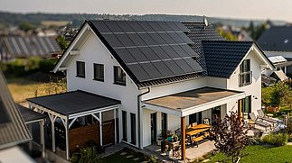 Modernes Einfamilienhaus mit Garten und vollflächiger Photovoltaik-Anlage auf dem Dach.