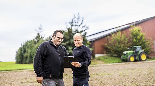 Mitarbeiter von Enatek im Gespräch mit Landwirt, Traktor im Hintergrund