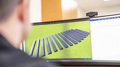 Techniker vor einem Monitor mit dem Bild einer Photovoltaik-Freiflächenanlage.