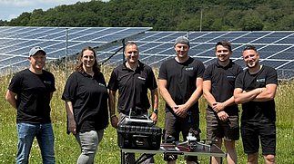 Gruppenfoto des enatek Service-Teams bei der CopterPro GmbH in Kirn: Die Gruppe steht auf einer Wiese vor Solarmodulen; im Vordergrund ein Tisch mit einer Drohne.