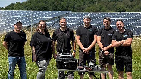 Gruppenfoto des enatek Service-Teams bei der CopterPro GmbH in Kirn: Die Gruppe steht auf einer Wiese vor Solarmodulen; im Vordergrund ein Tisch mit einer Drohne.