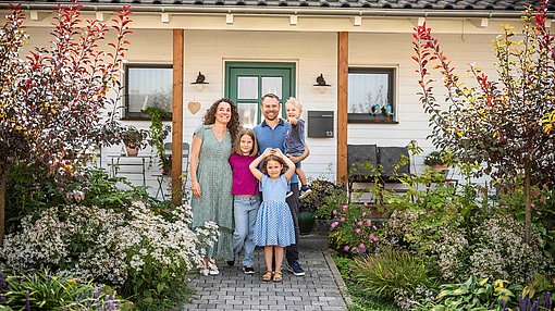 Eine Ehepaar mit drei Kindern steht vor einem Eigenheim