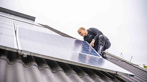 Techniker installiert ein Solarmodul auf einem Hausdach.